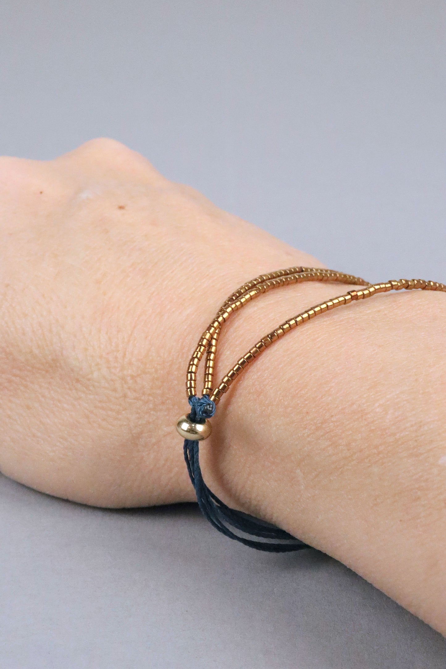 Gros plan du bracelet Abbie porté, en perles du Japon dorées montées sur des cordons en nylon couleur vert canard
