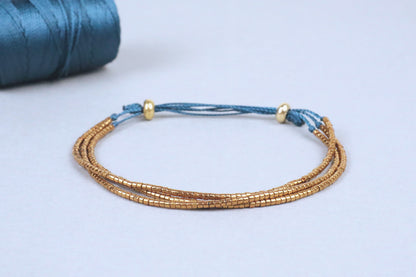 Gros plan du bracelet Abbie, en perles du Japon dorées montées sur des cordons en nylon couleur vert canard