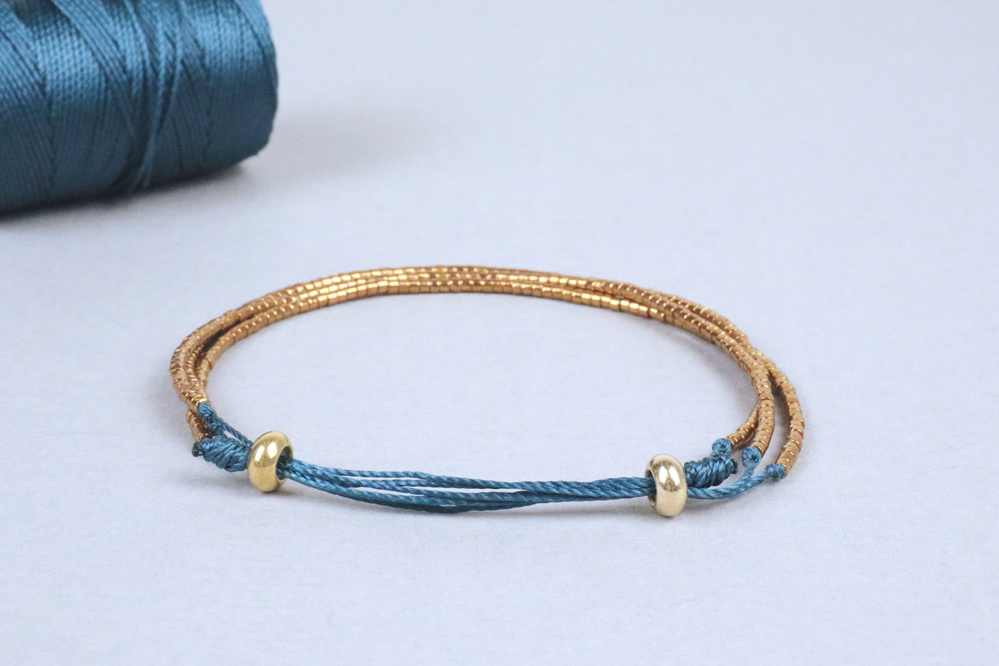 Gros plan du bracelet Abbie, en perles du Japon dorées montées sur des cordons en nylon couleur vert canard