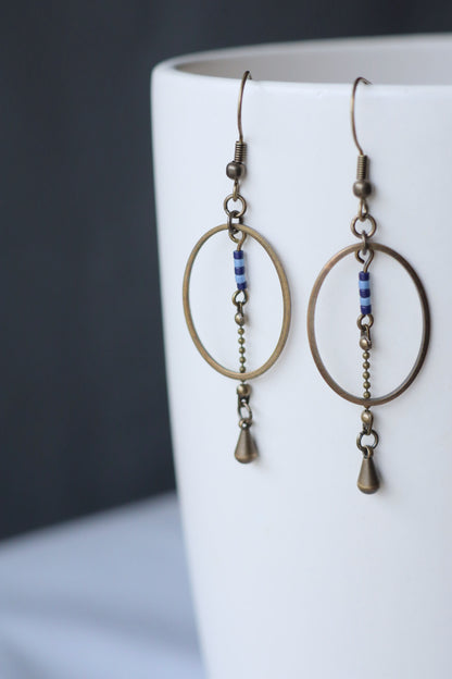 Boucles d'oreilles pendantes, modèle Alana, ovales en laiton avec des perles bleues accrochées sur un vase de porcelaine blanche