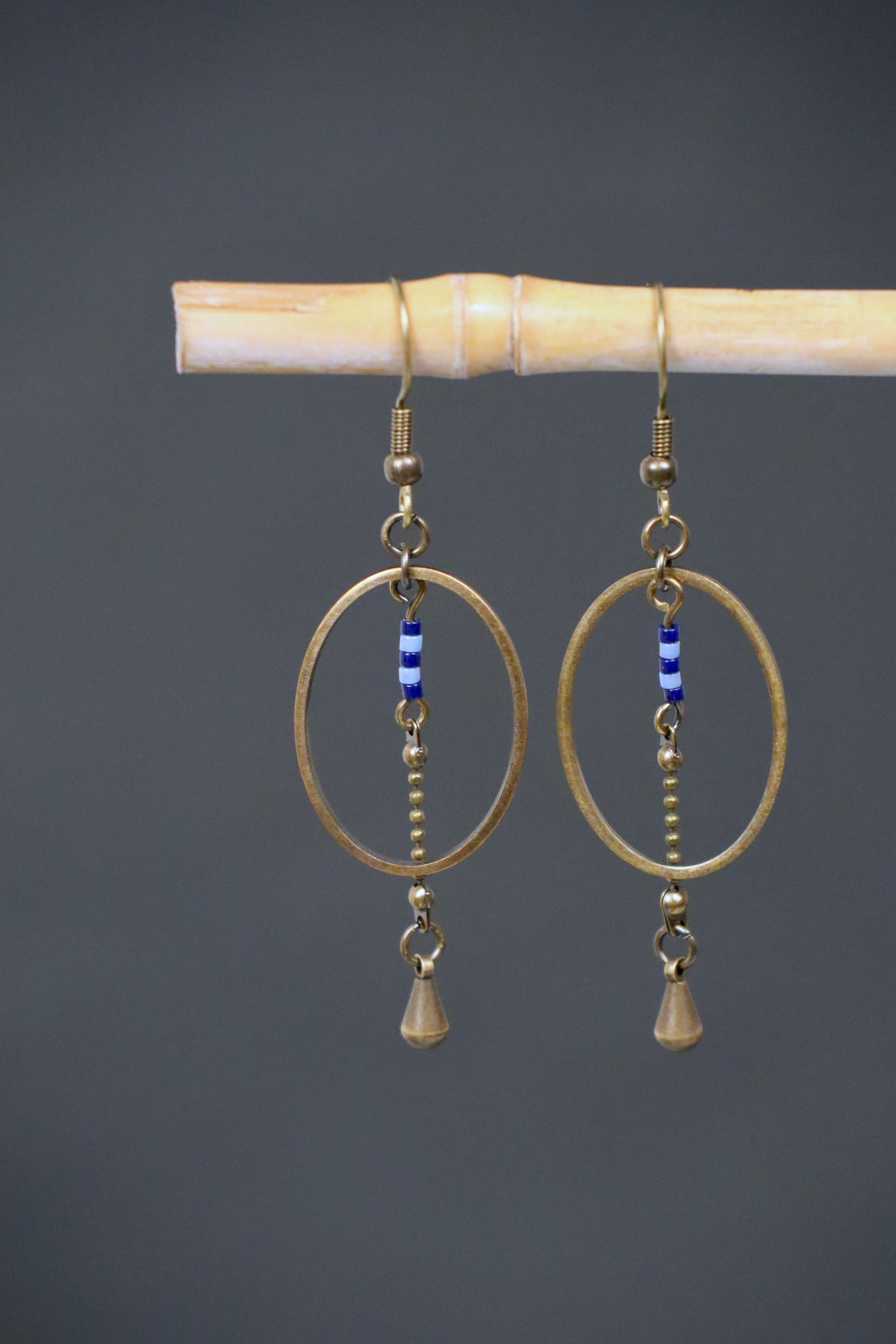 Gros plan des boucles d'oreilles pendantes, modèle Alana, ovales en laiton avec des perles bleues